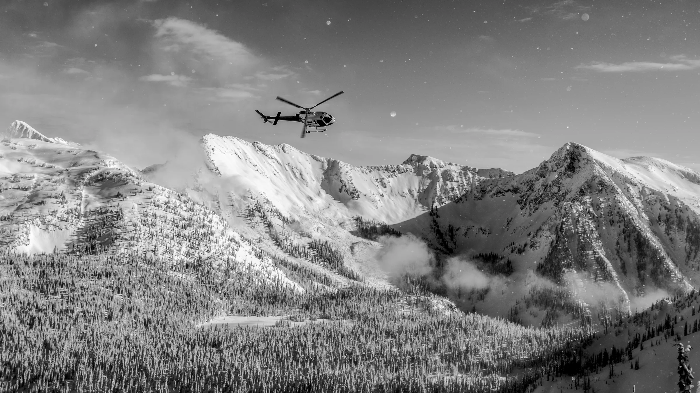 Helicopter flying over a snow-covered mountain ridge in the BC Interior backcountry